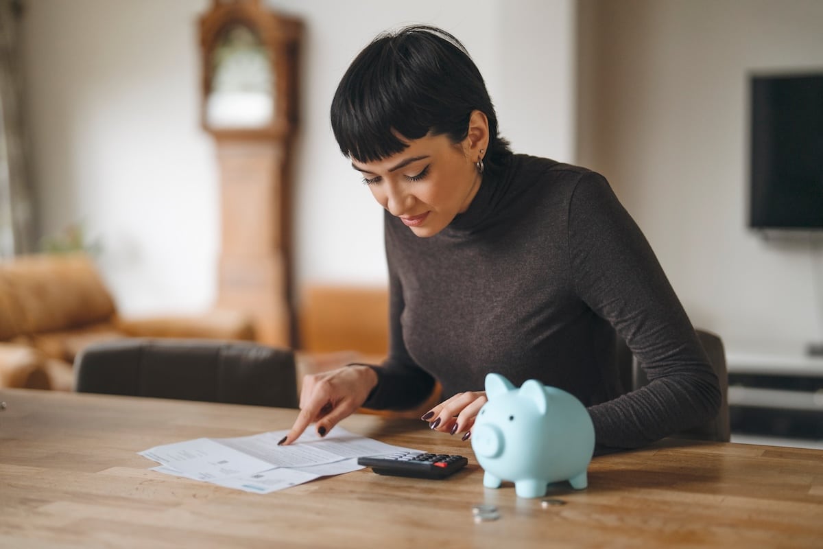 Woman managing finances at home with piggy bank and calculator during daytime